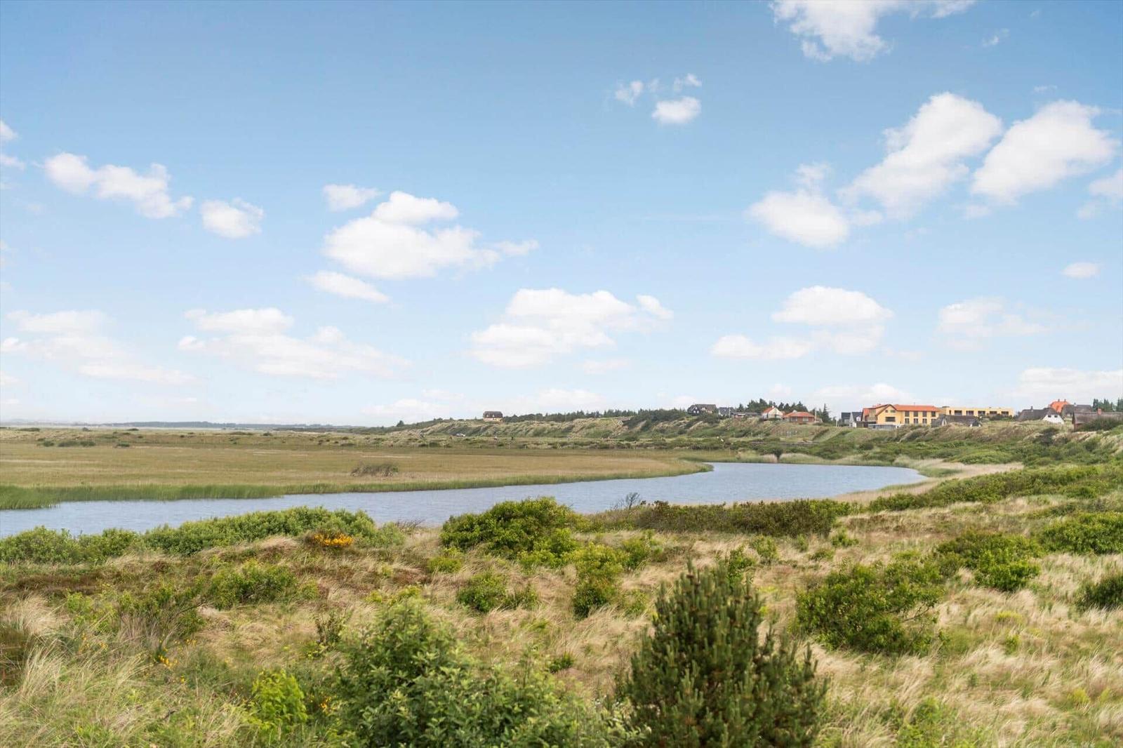 Weitläufiger Blick auf eine Moorelandschaft mit einem See und Häusern am Horizont.