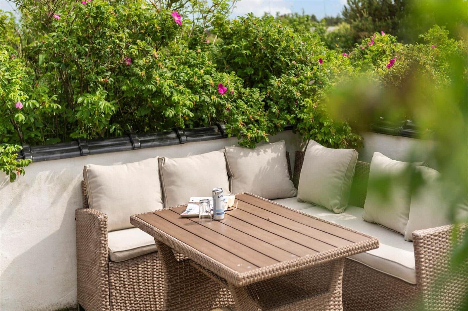 Terrasse mit Sitzbank, Tisch und Pflanzen im Hintergrund.