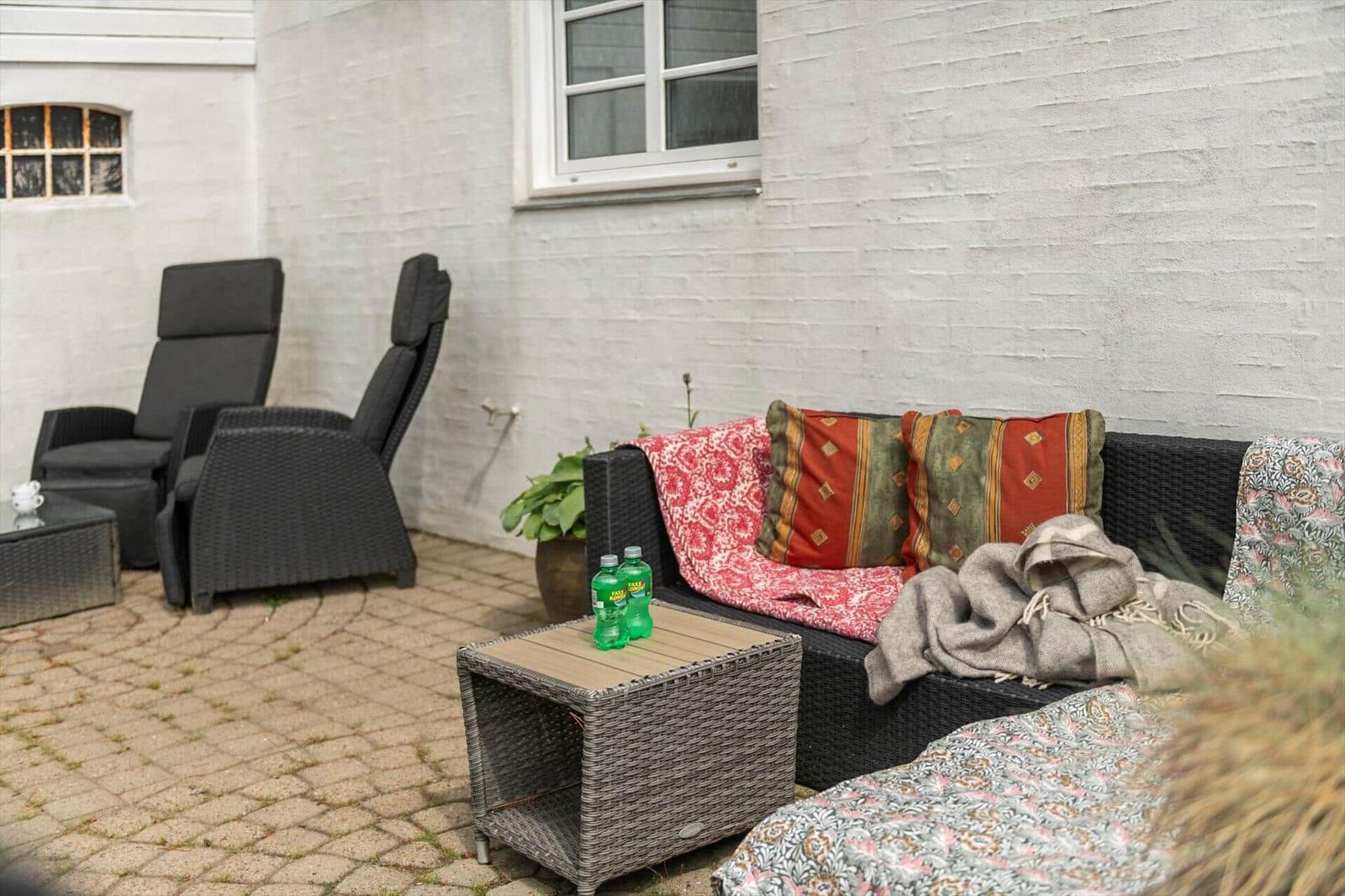Außenbereich mit Sofa, Sitzmöbeln und Tisch. Hintergrund: weiße Wand und Fenster.