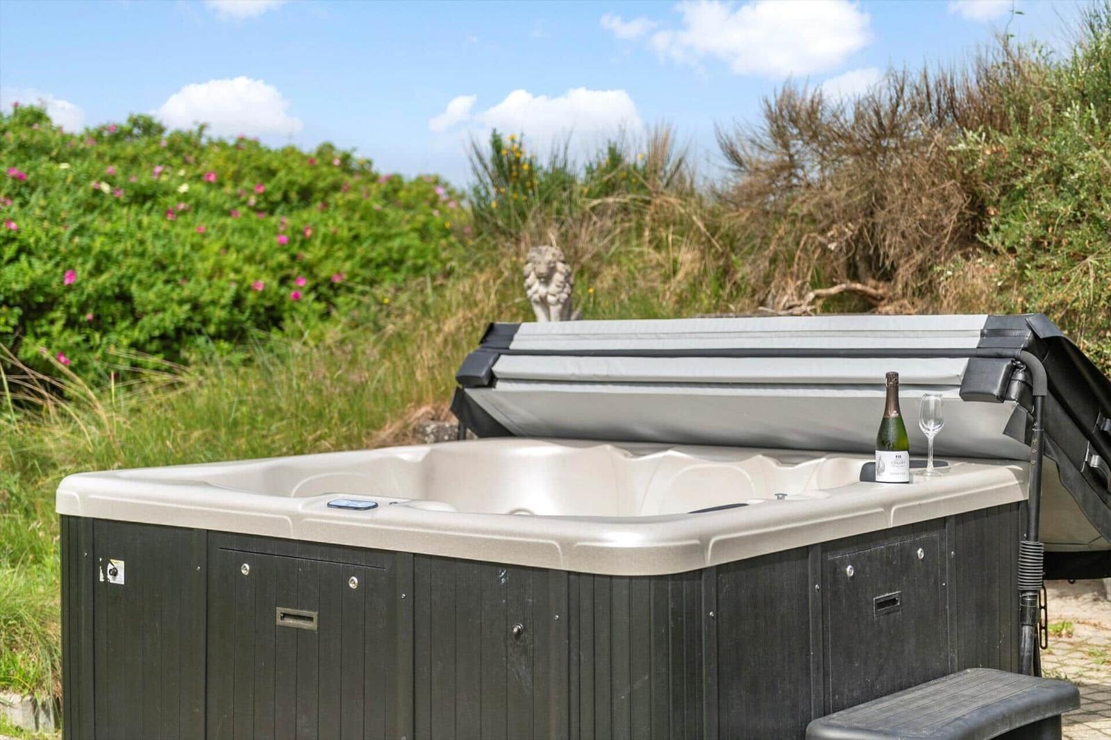 Ein Whirlpool mit geöffneter Abdeckung, daneben steht eine Flasche und ein Glas.
