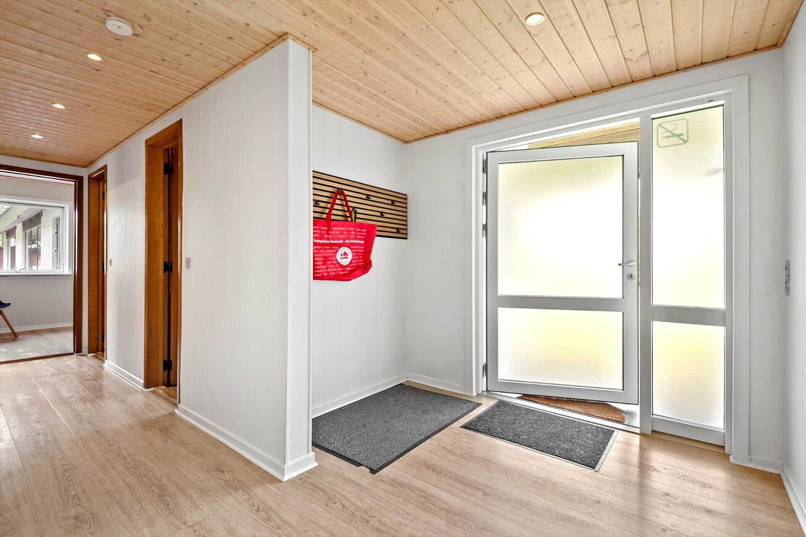Eingangsbereich mit Holzboden, weißen Wänden und einer Glastür.