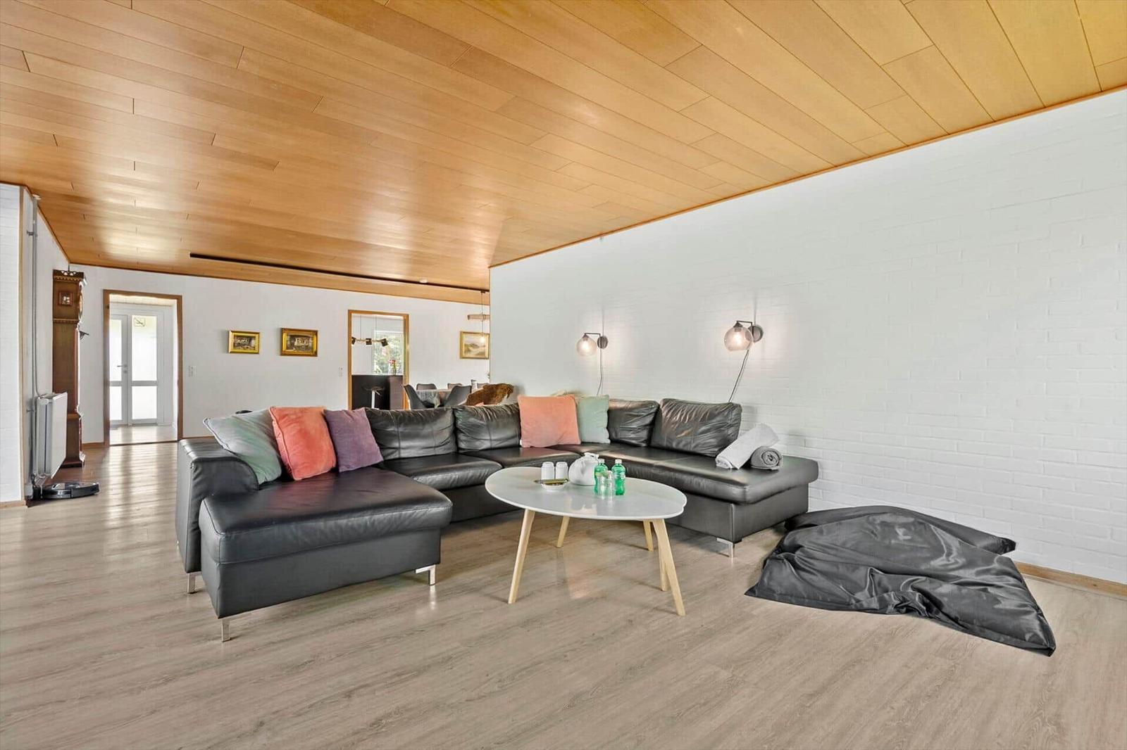 Großer Wohnbereich mit Leder-Sofa, runden Tisch und Holzdecke.