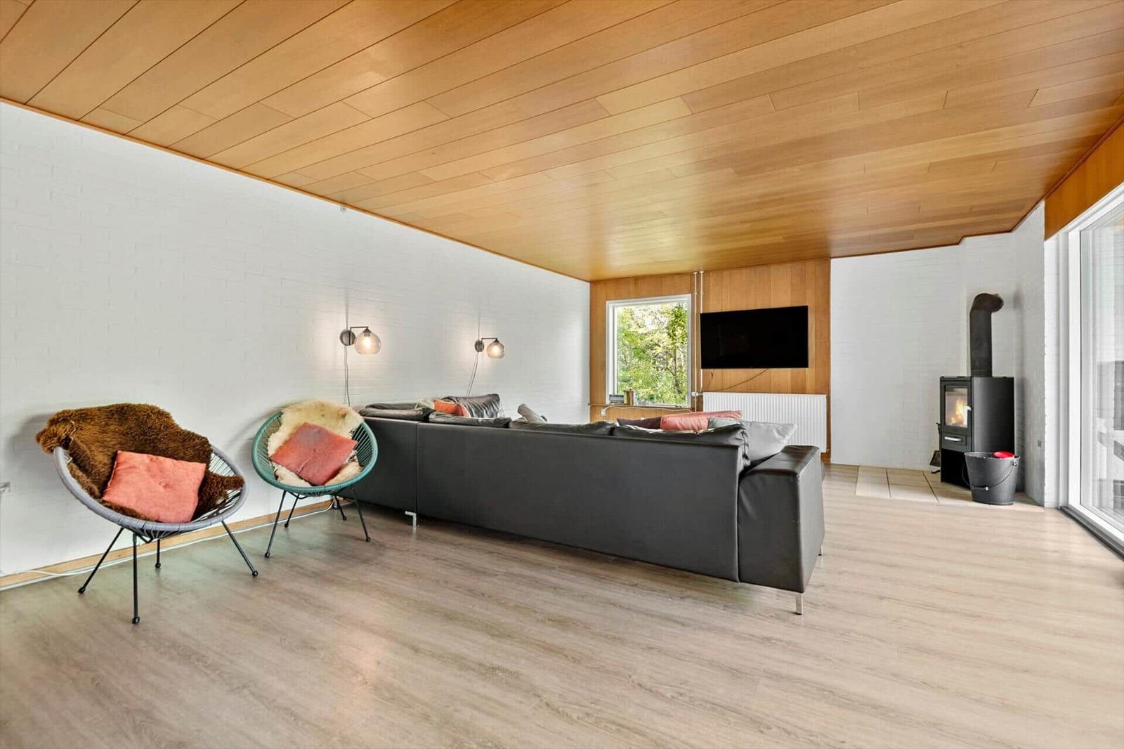 Wohnzimmer mit Sofa, zwei Sesseln, Holzdecke und Kaminofen.