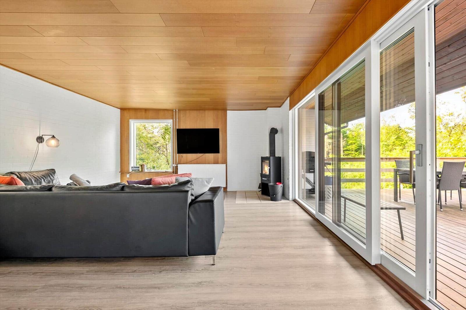Wohnzimmer mit Sofa, Kamin und Terrasse. Holzdecke und boden.