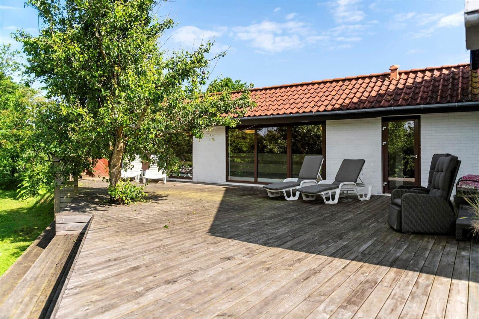 Terrasse mit Liegen und Sitzmöbeln vor einem Haus mit rotem Dach.