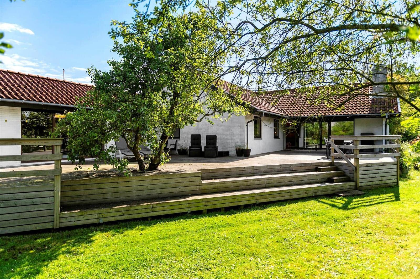 Wohnhaus mit Holzterrasse, Garten und Baum. Außenbereich mit Sitzgelegenheiten.
