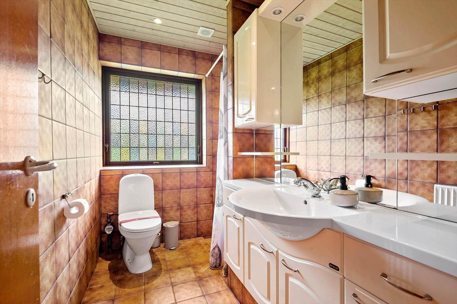 Badezimmer mit Toilette, Waschbecken und Fenster mit getöntem Glas.
