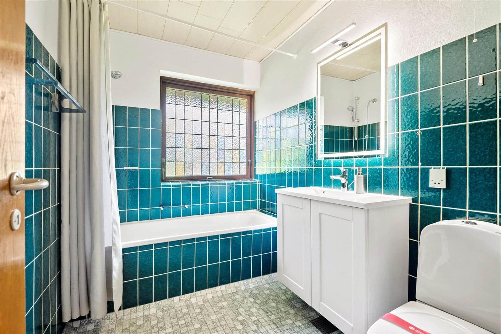 Badezimmer mit Badewanne, Waschbecken und Toilette. Wände mit türkisfarbenen Fliesen.