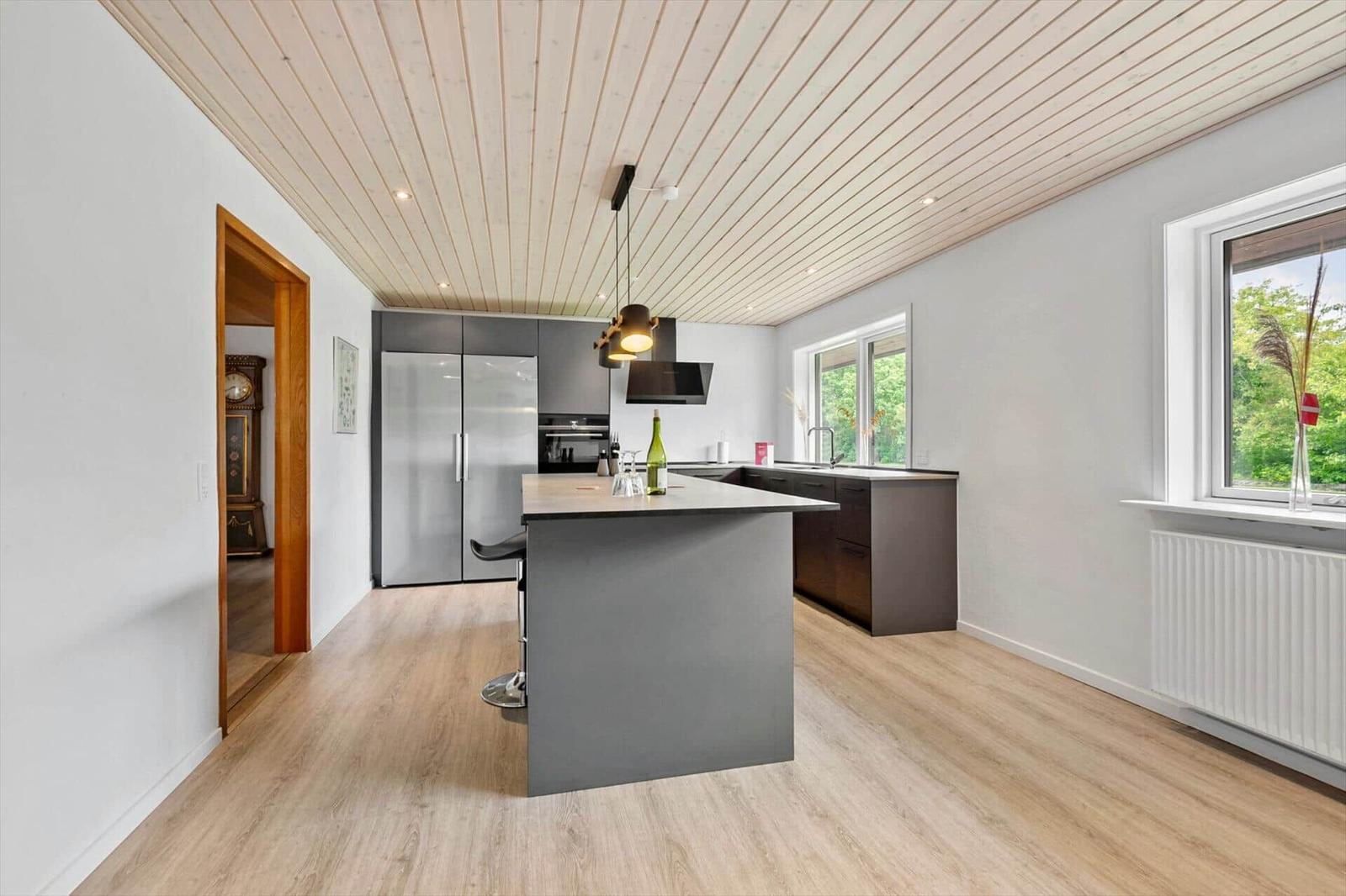 Moderne Küche mit Kücheninsel, Edelstahl-Kühlschrank und Holzdecke.