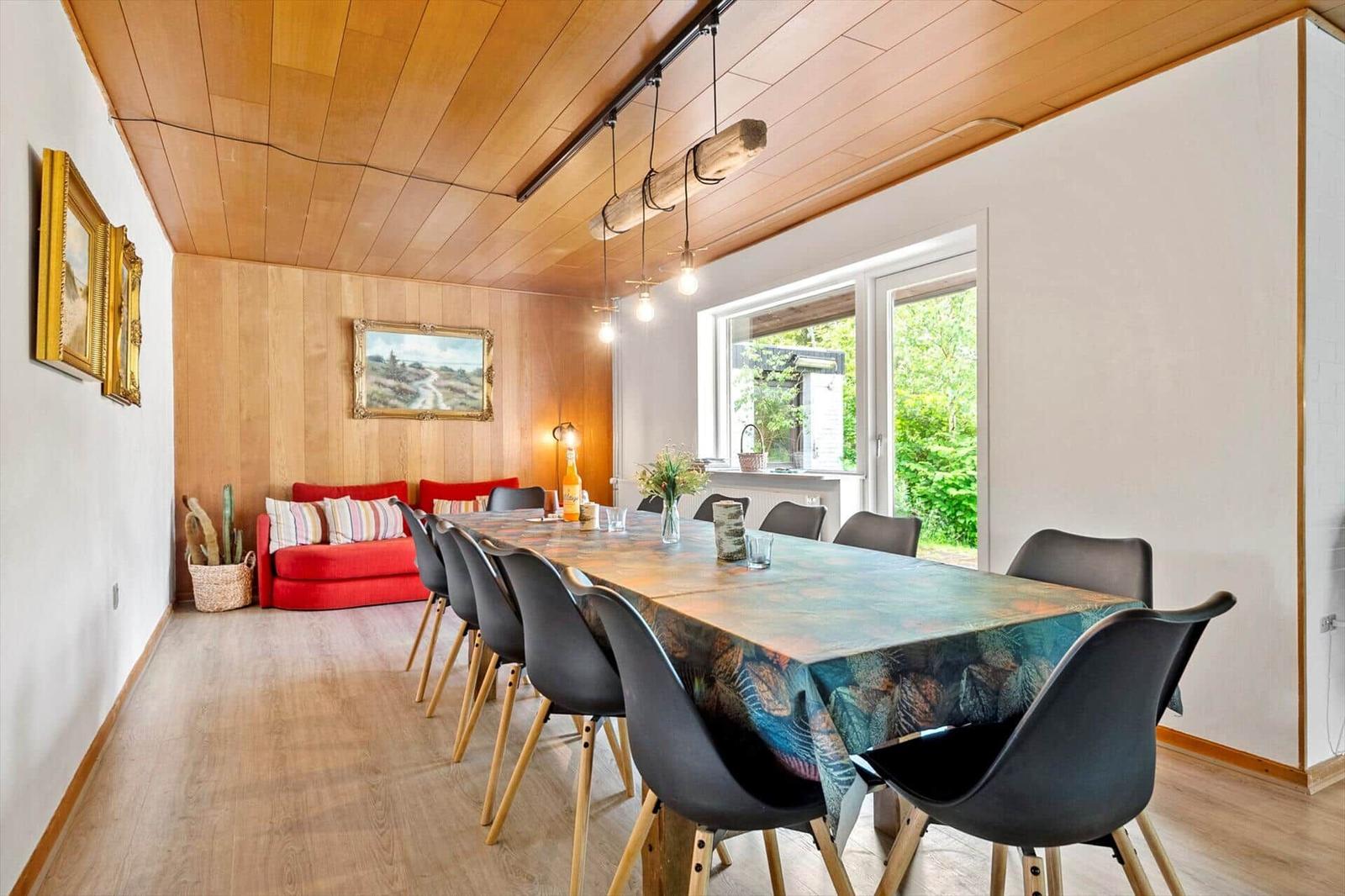 Essbereich mit langem Tisch, schwarzen Stühlen und rotem Sofa an der Wand.
