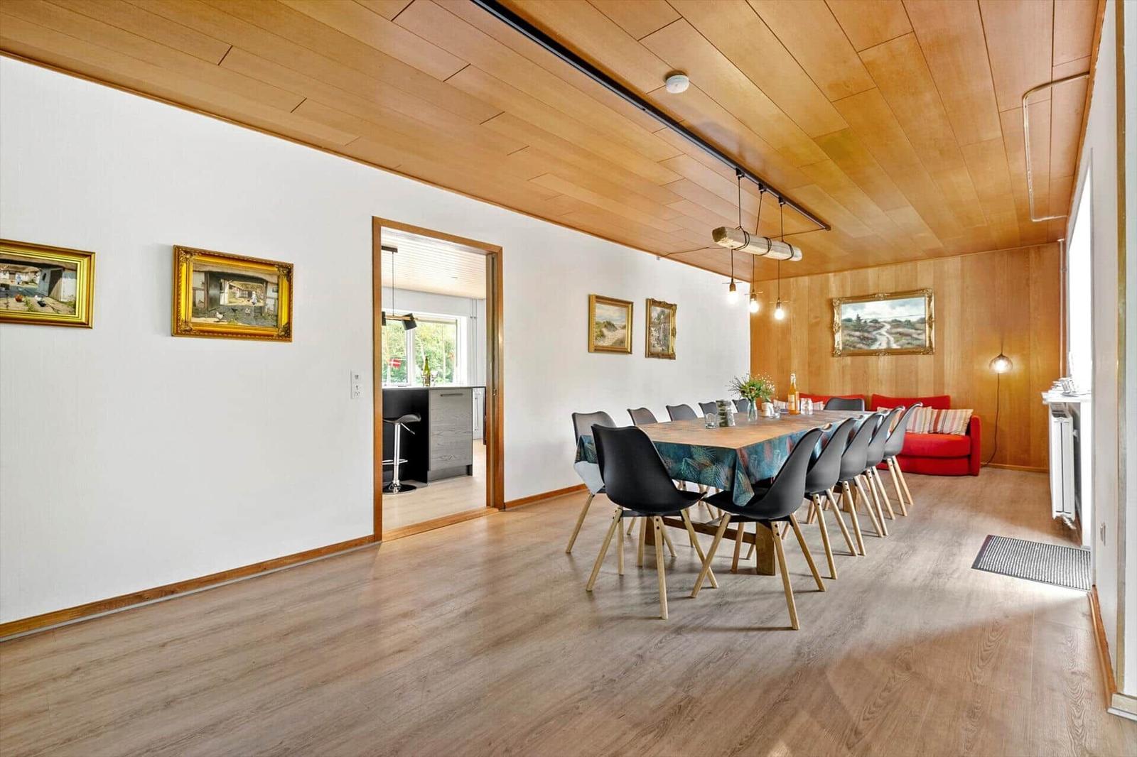 Esszimmer mit langem Tisch, schwarzen Stühlen und rotem Sofa. Holzdecke und -boden.