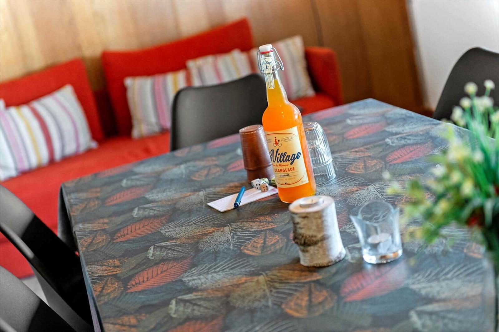 Tisch mit Flasche, Gläsern und Dekoration vor rotem Sofa.