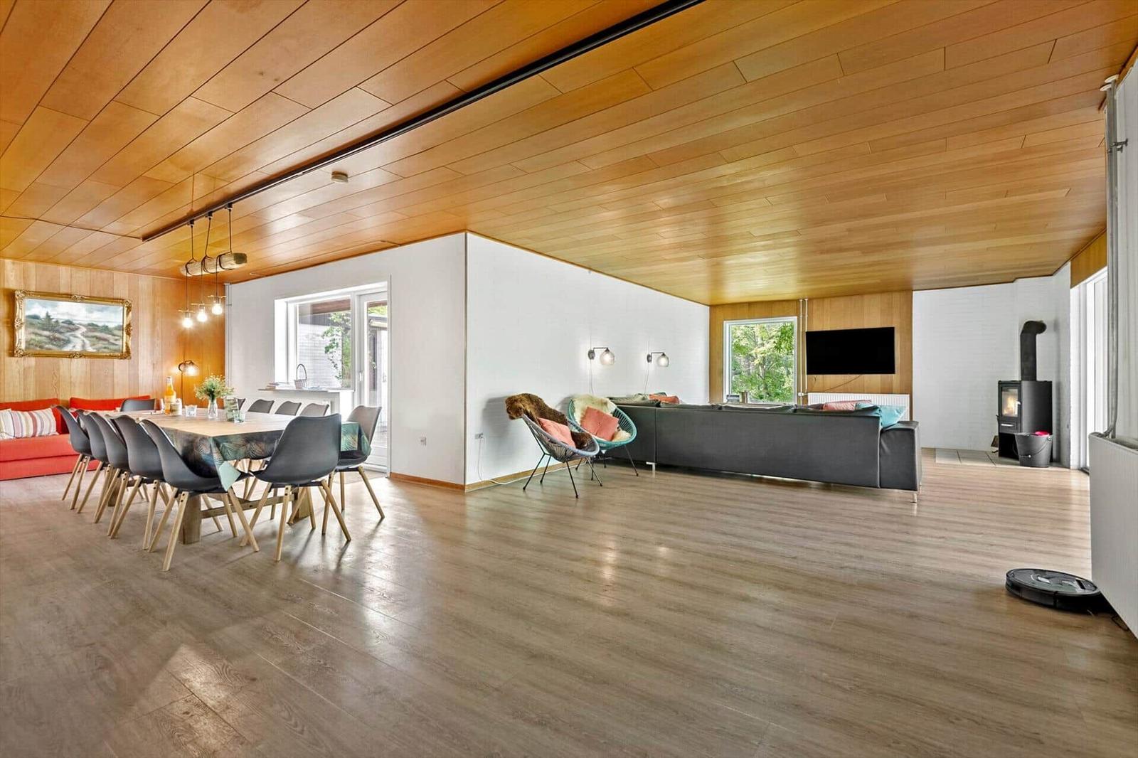 Großer Wohnbereich mit Essbereich, Sofa und Kaminofen. Holzdecke und -boden.