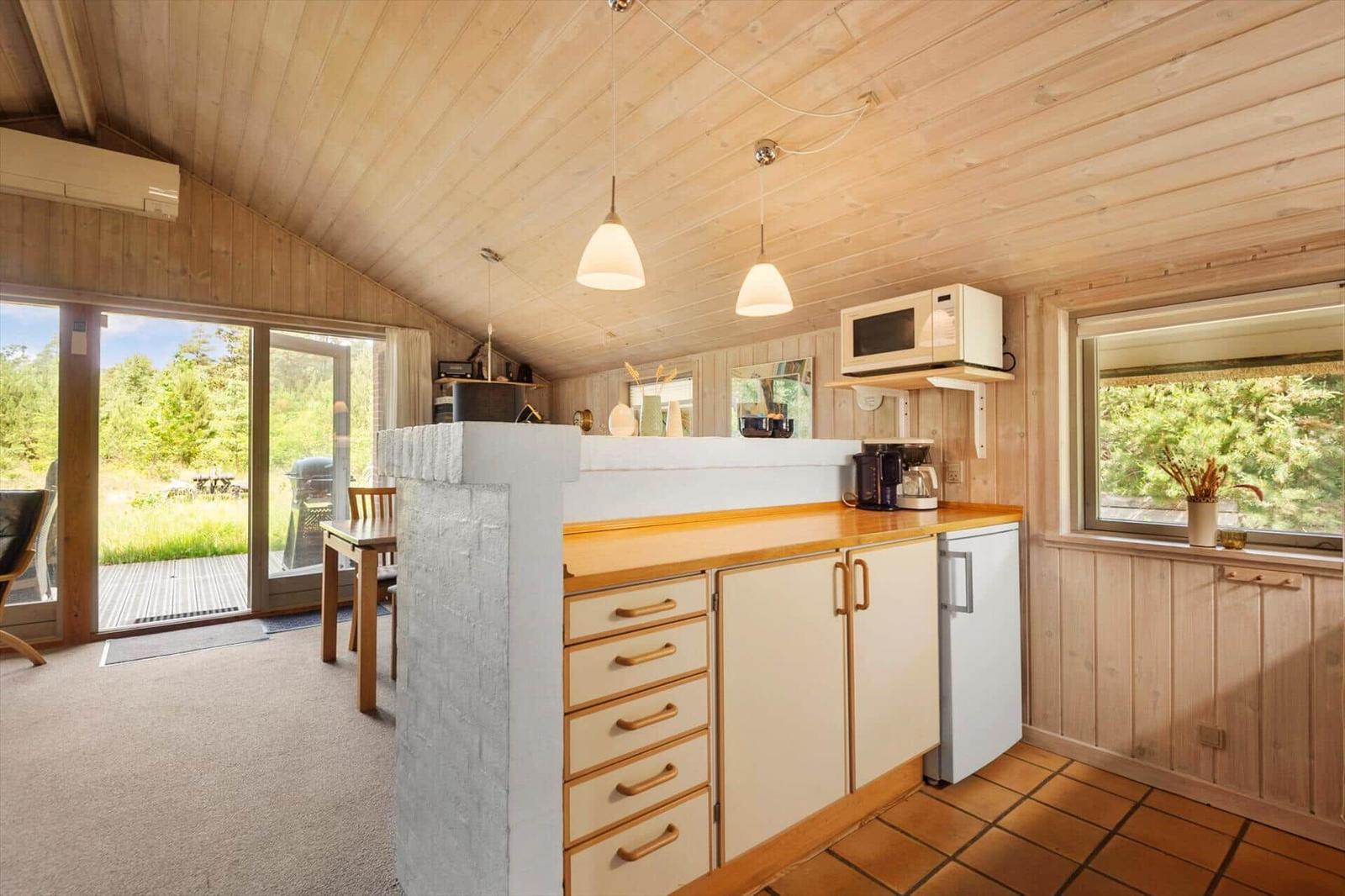Küche mit Holzwand, Arbeitsplatte und Fenster. Mikrowelle und Kühlschrank sind vorhanden.