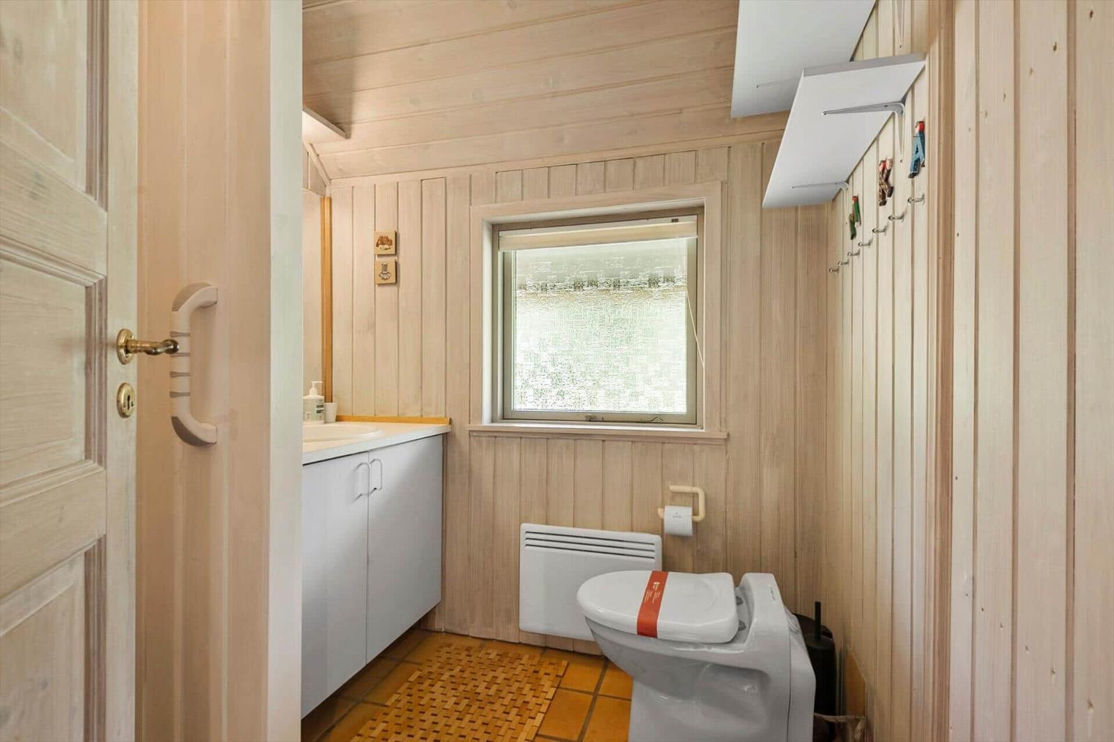 Badezimmer mit Holzwand, Toilette, Waschbecken und Fenster.