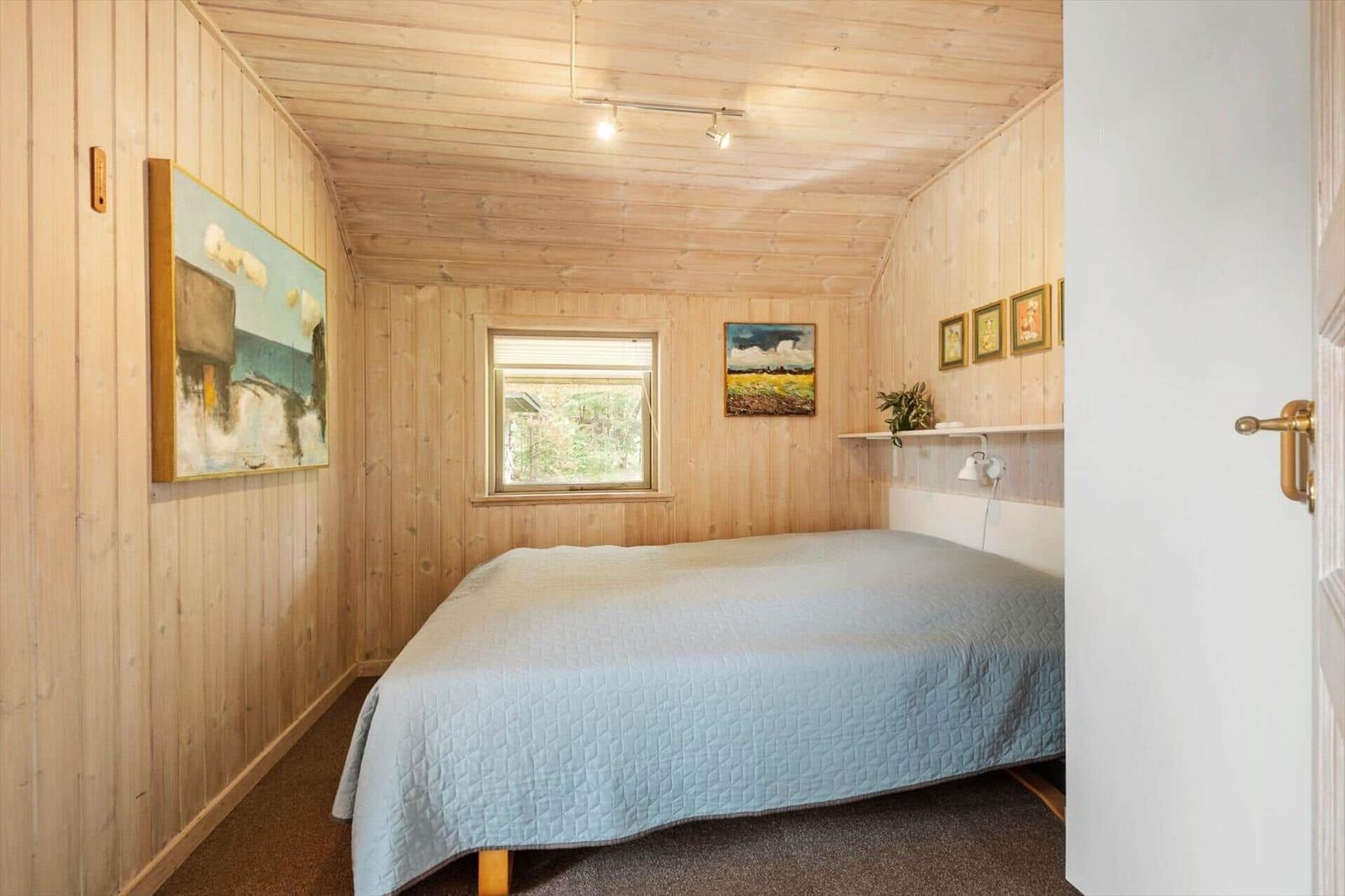 Schlafzimmer mit Holzwänden, Bett und Fenster. Gemälde an den Wänden.