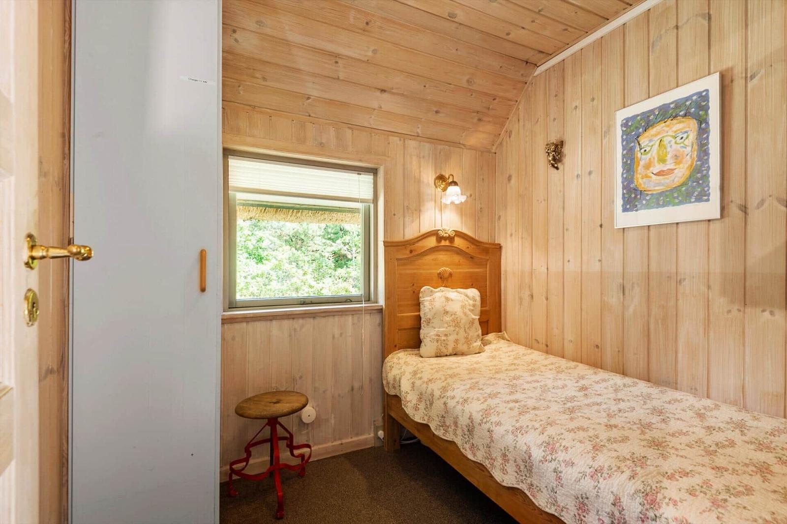 Ein Schlafzimmer mit Holzwand, Bett, Fenster und Stuhl.