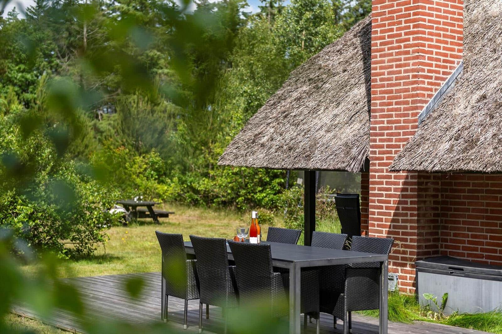 Außenbereich mit Tisch, Stühlen und Dach über dem Tisch. Hintergrund: Grünfläche und Baum.