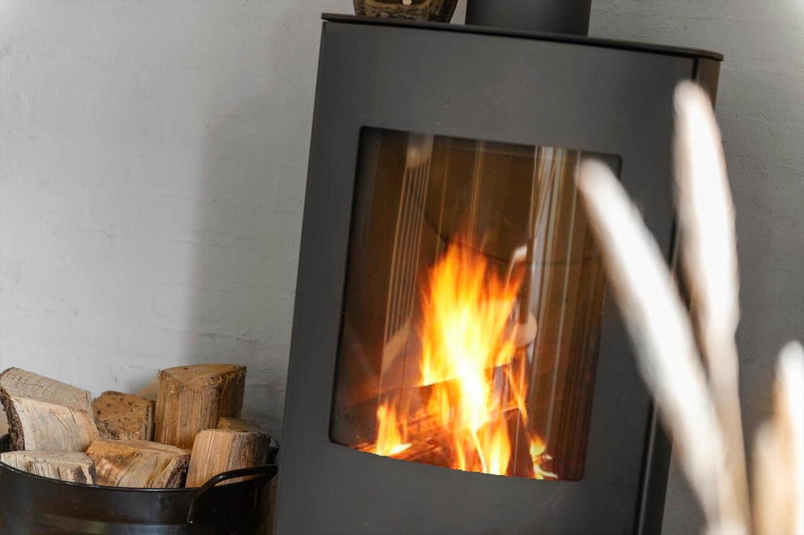 Ein schwarzer Kaminofen mit brennendem Holz, daneben ein Eimer mit Brennholz.
