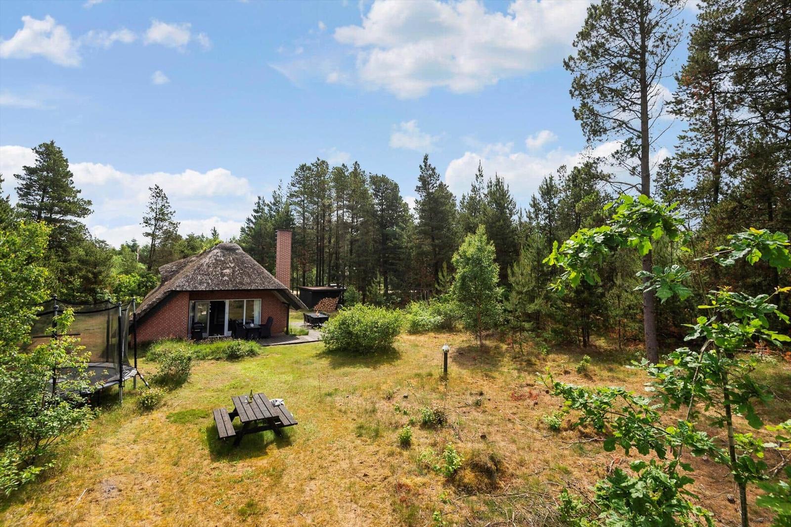 Hütte mit Strohdach und Garten in Waldnähe. Picknicktisch und Trampolin sind vorhanden.