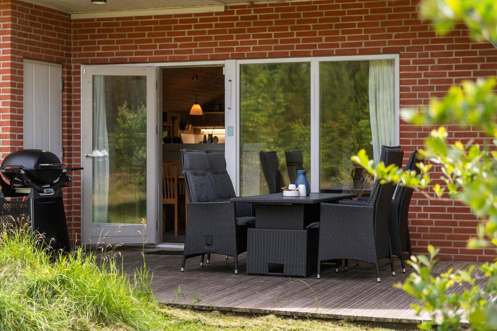 Terrasse mit Sitzgruppe, Grill und Blick ins Haus. Holzdeck und rote Ziegelwand.