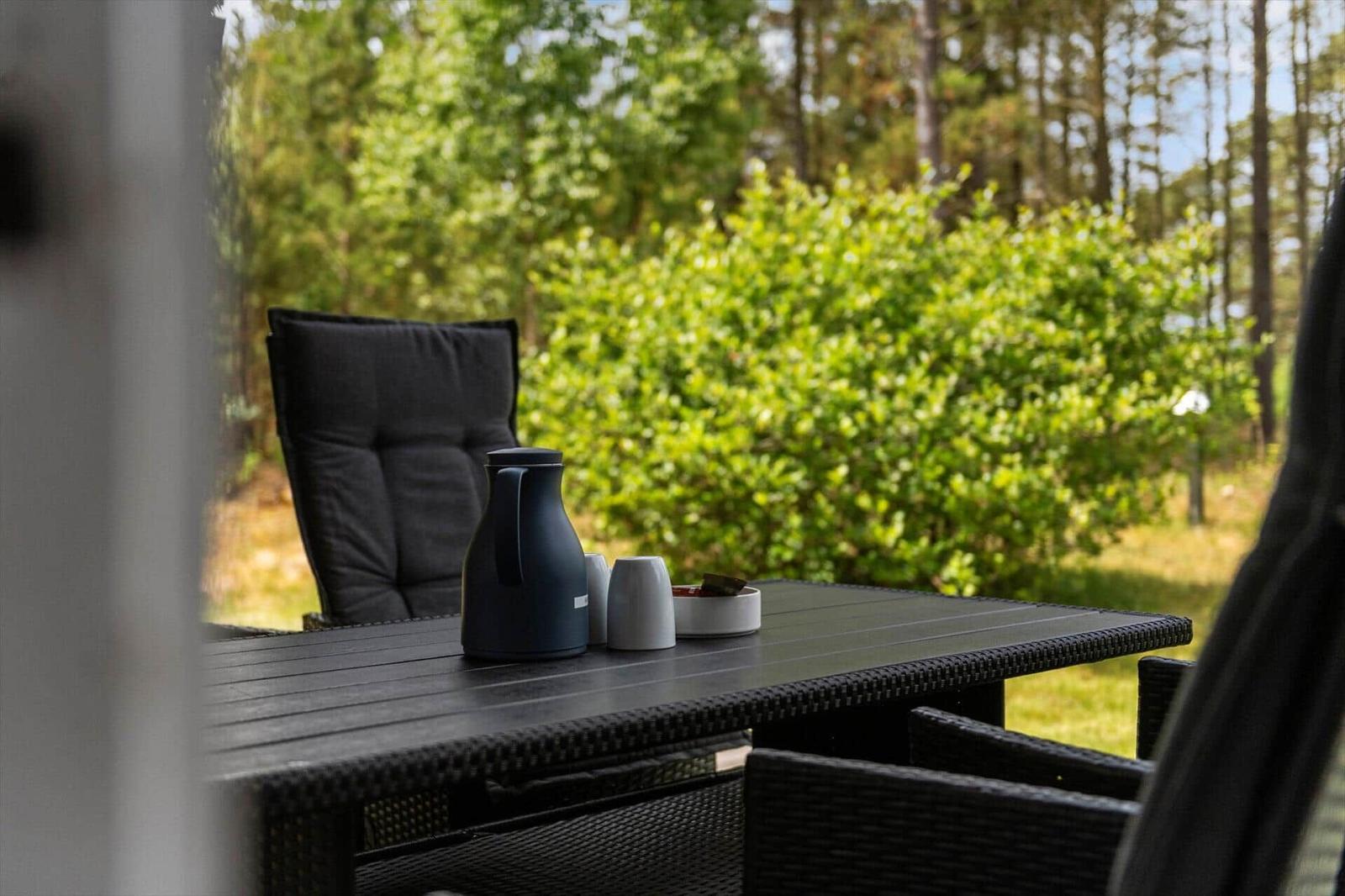 Außenbereich mit Tisch, Stühlen und einer Thermoflasche.