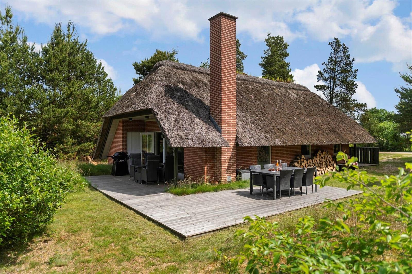 Haus mit Strohdach, Holzterrasse und Grillplatz im Grünen.