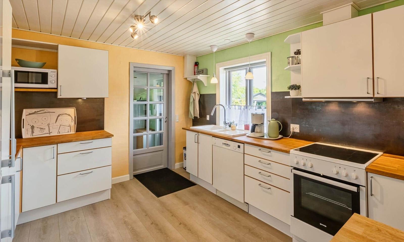 Kitchen with white cabinets, wooden countertops, and window. Dishwasher, stove, and refrigerator visible.