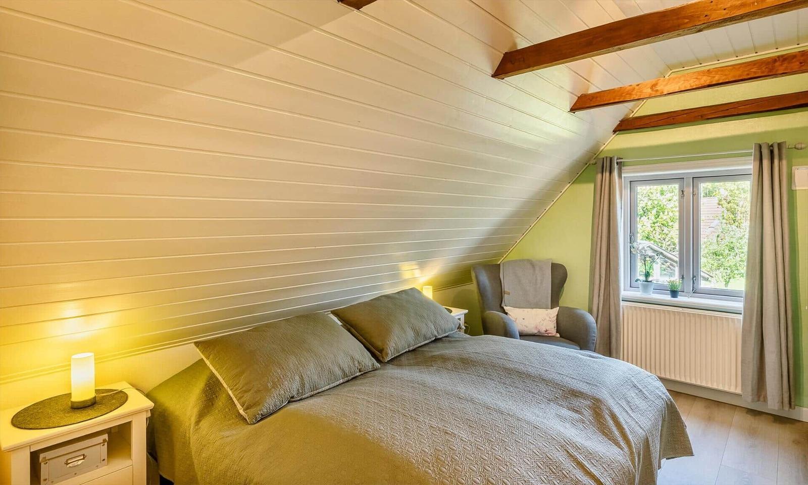 Bedroom with sloped ceiling, bed, nightstand, and window with view outside.