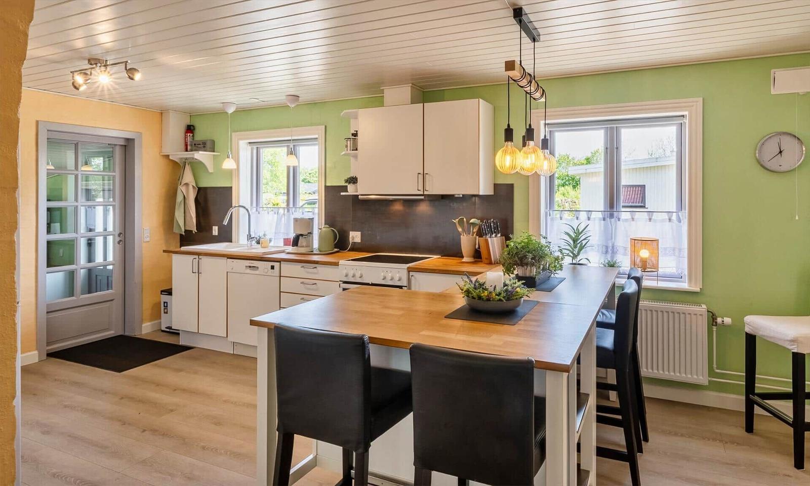 Kitchen with wooden island, white cabinets, and green walls. Windows with view outside.