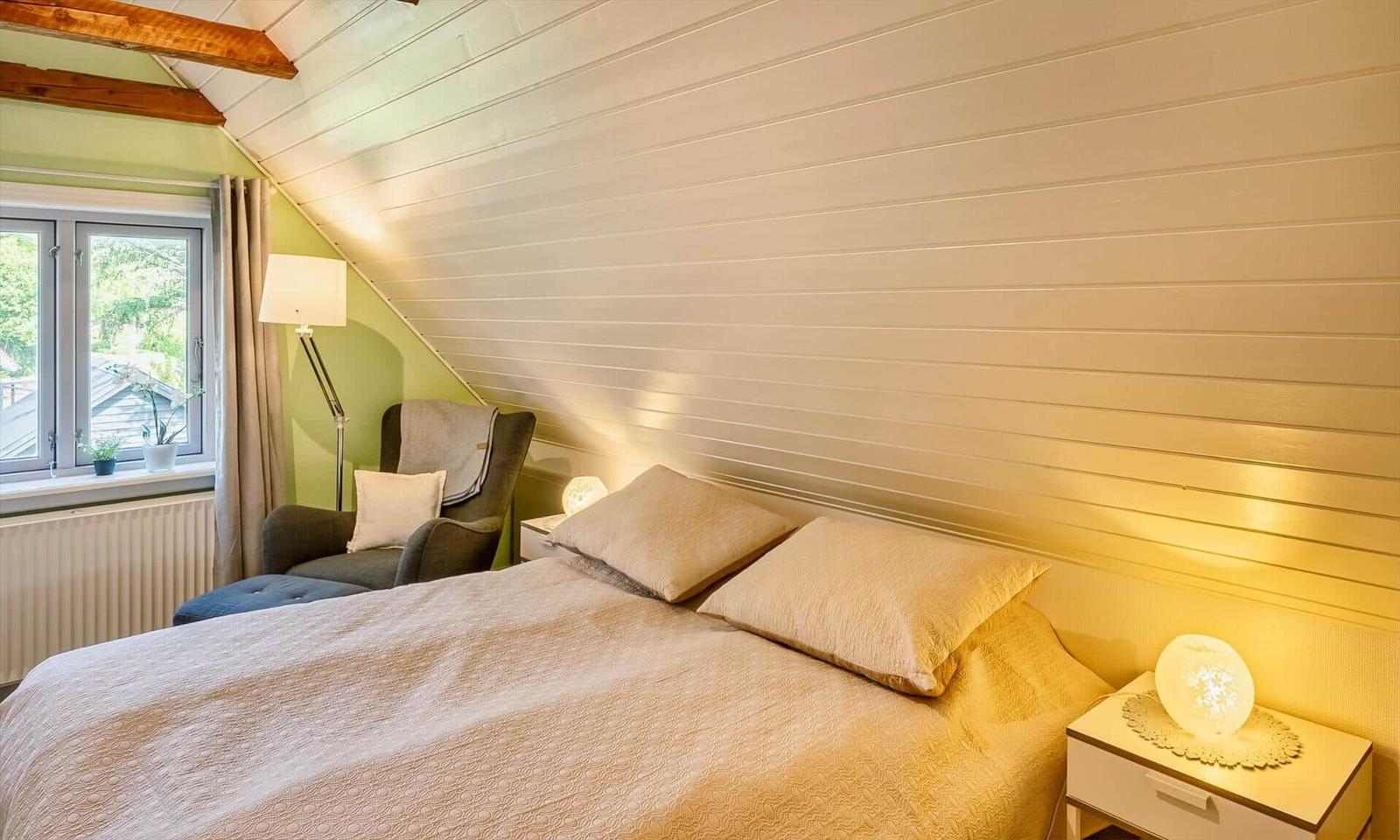 Bedroom with bed, nightstand, and armchair under sloped ceiling.