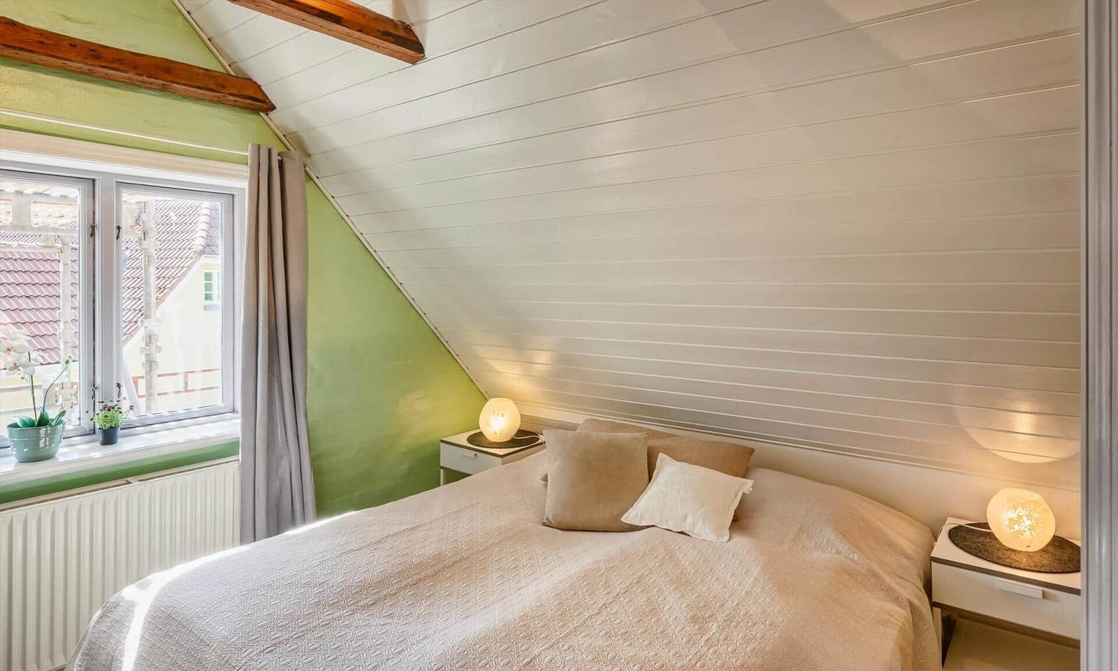 Bedroom with sloped ceiling, bed, nightstands, and window with view.