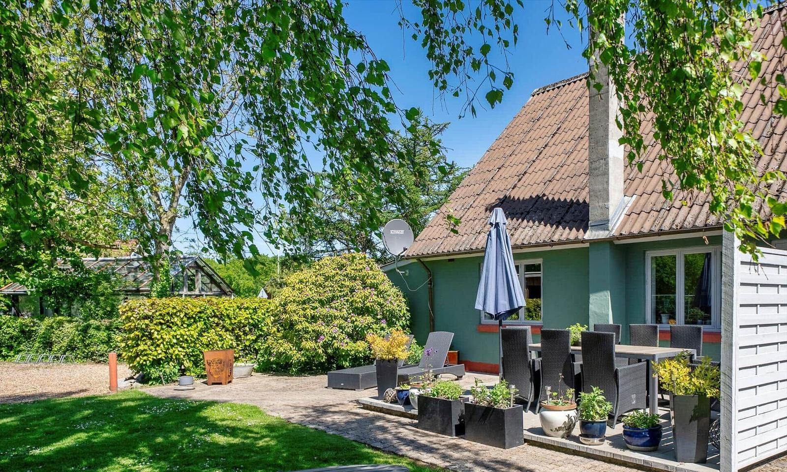 Green garden with terrace, seating, and satellite dish on the house wall.