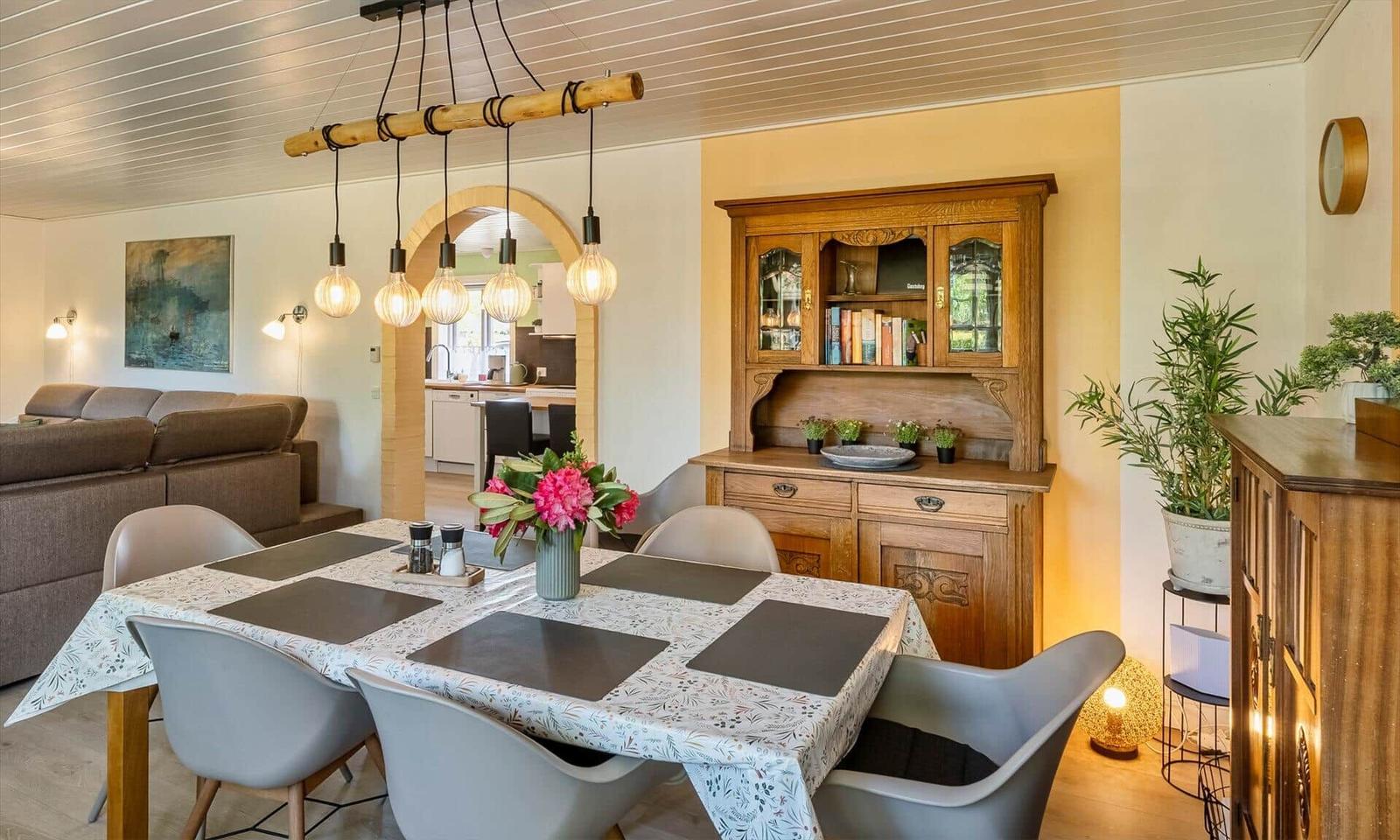 Dining room with table, chairs, and wooden cabinet. Passage to kitchen and living room.