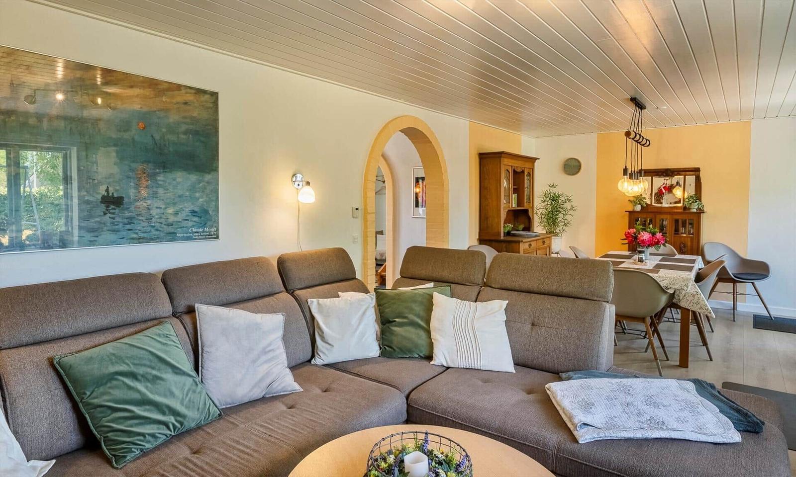 Living room with sofa, cushions, and dining area. Wall art and arch visible.