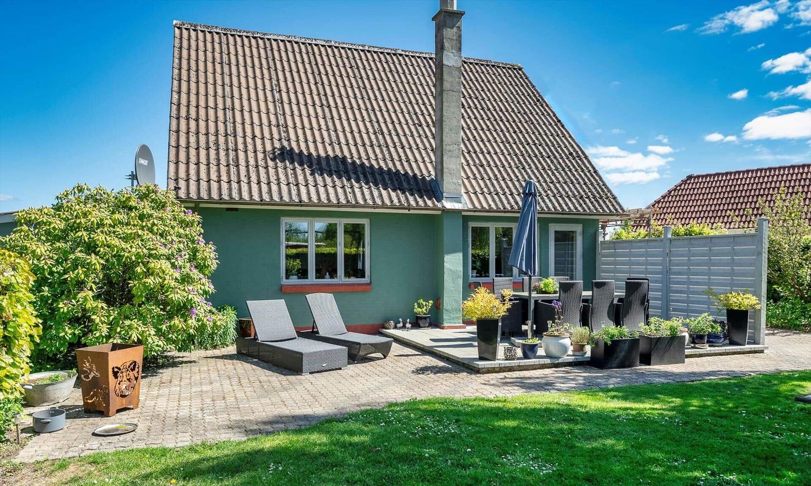 Green house with terrace, loungers, and garden. Visible: satellite dish, plants, and grill area.