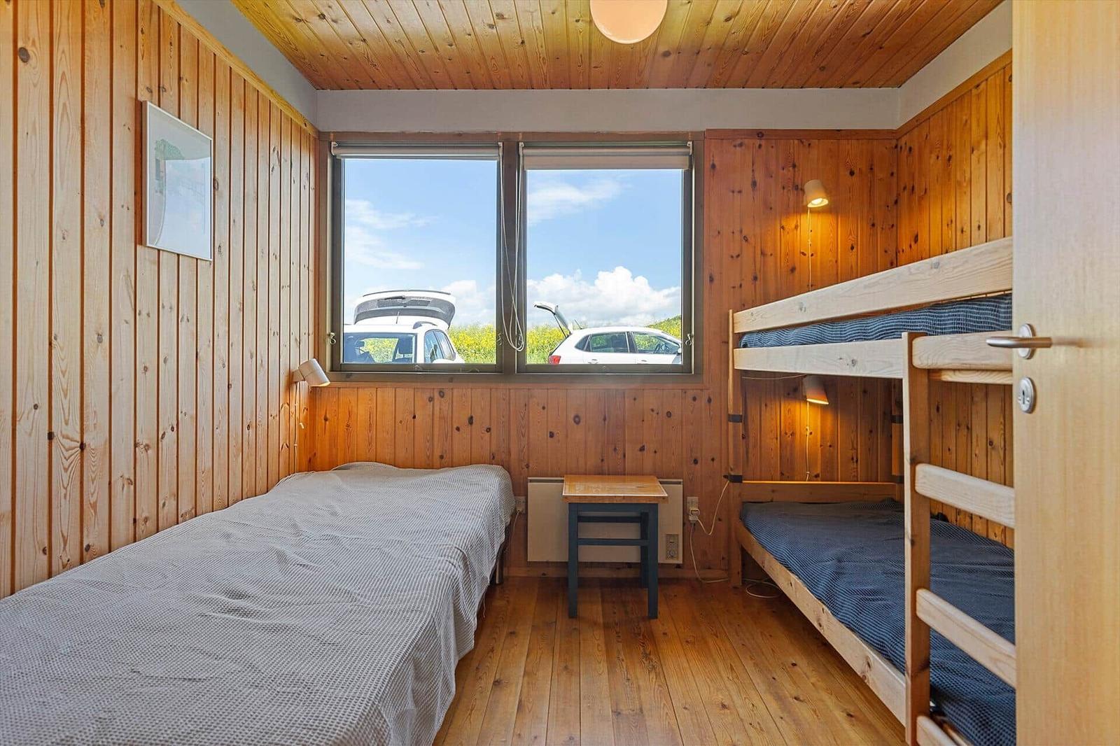 Room with double bed and bunk bed, wooden walls and window overlooking parking lot.