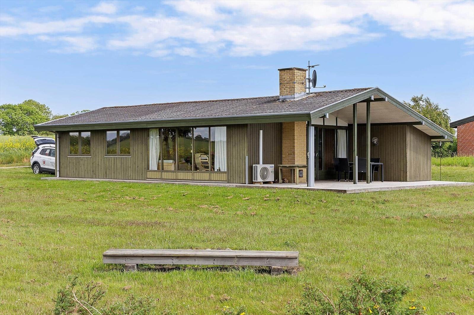 A house with wooden siding, large windows, and a patio with a table and chairs.