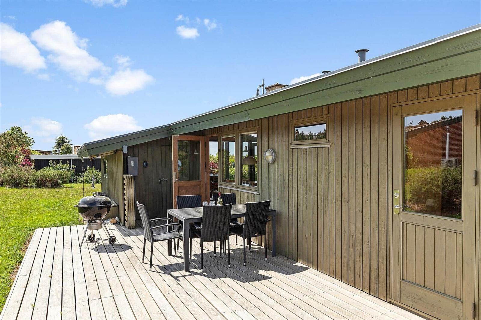 Deck with table, chairs, and grill. Wooden house with windows and door.