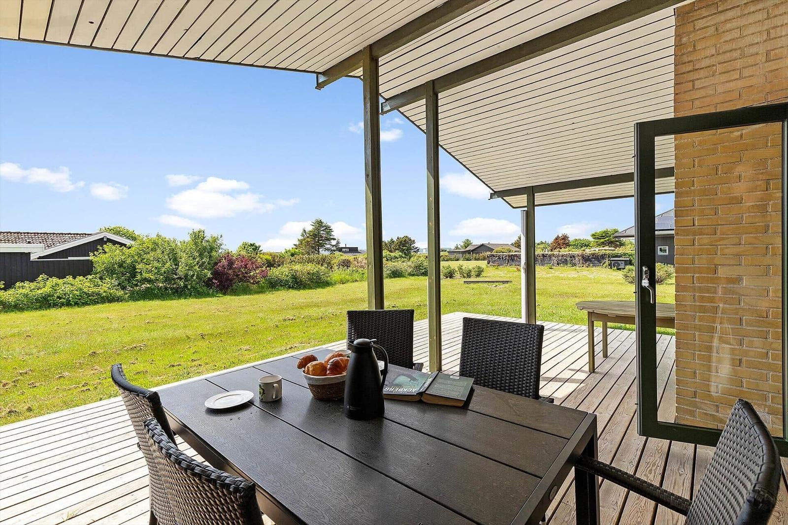 Patio with table and chairs, view of green lawn and sky.