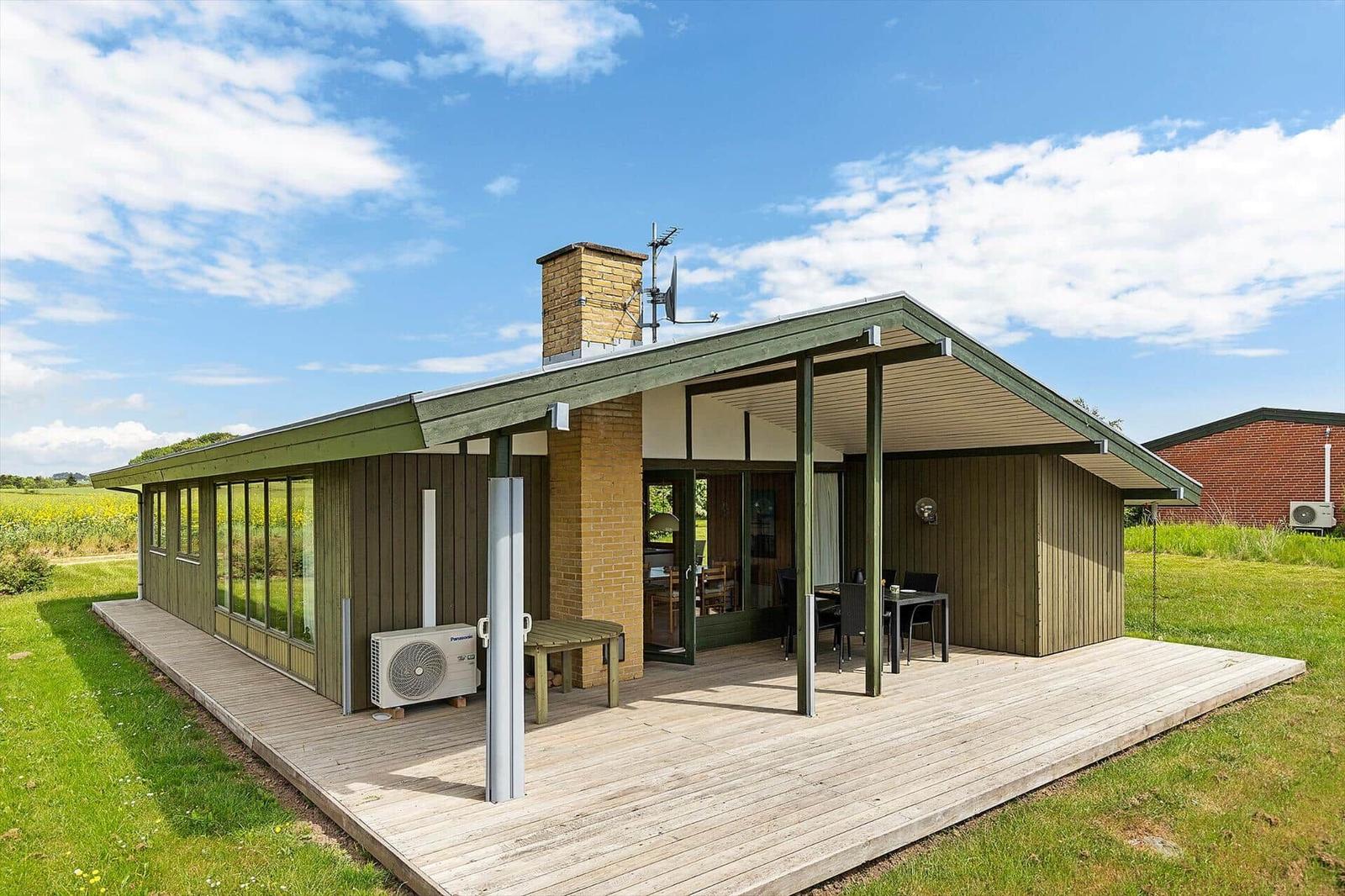 Modern cabin with terrace, garden, and field view under blue sky.