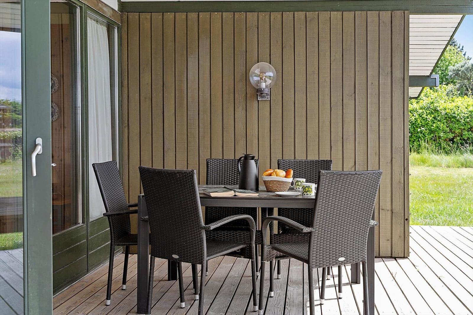 Terrace with table and four chairs, wooden wall and garden door.