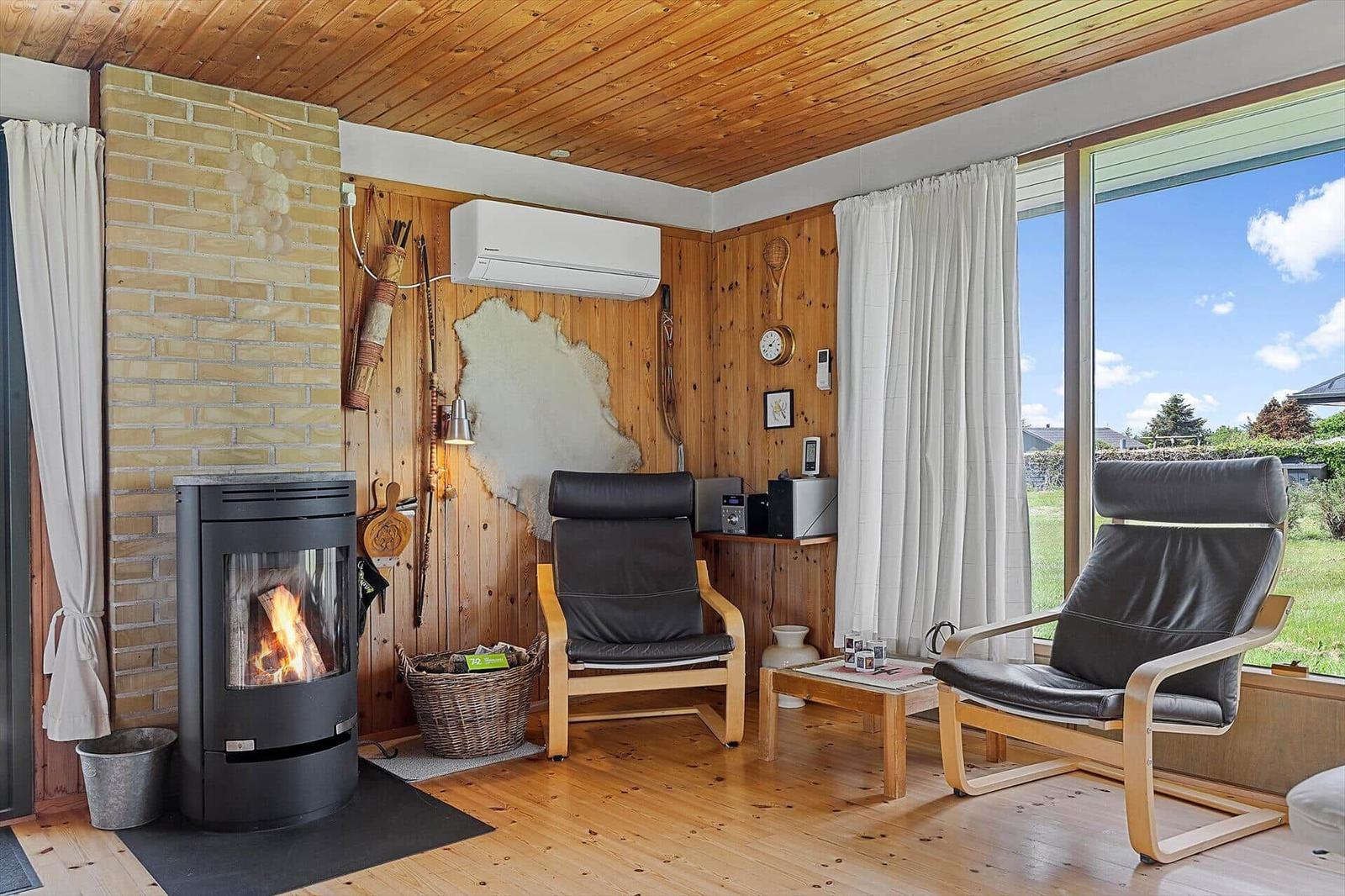 Room with fireplace, two chairs, and large window overlooking green area.