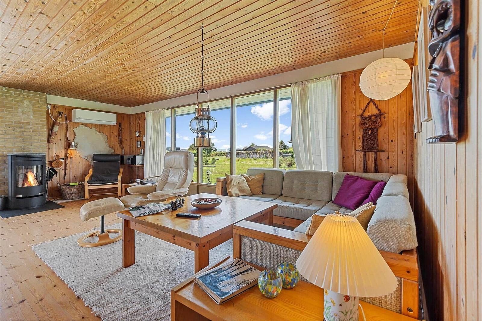 Living room with wooden ceiling, sofa, fireplace, and large window with view of the landscape.
