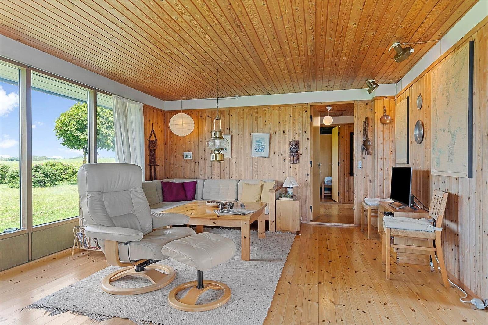 Living room with wooden ceiling, sofa, recliner, and view of field.