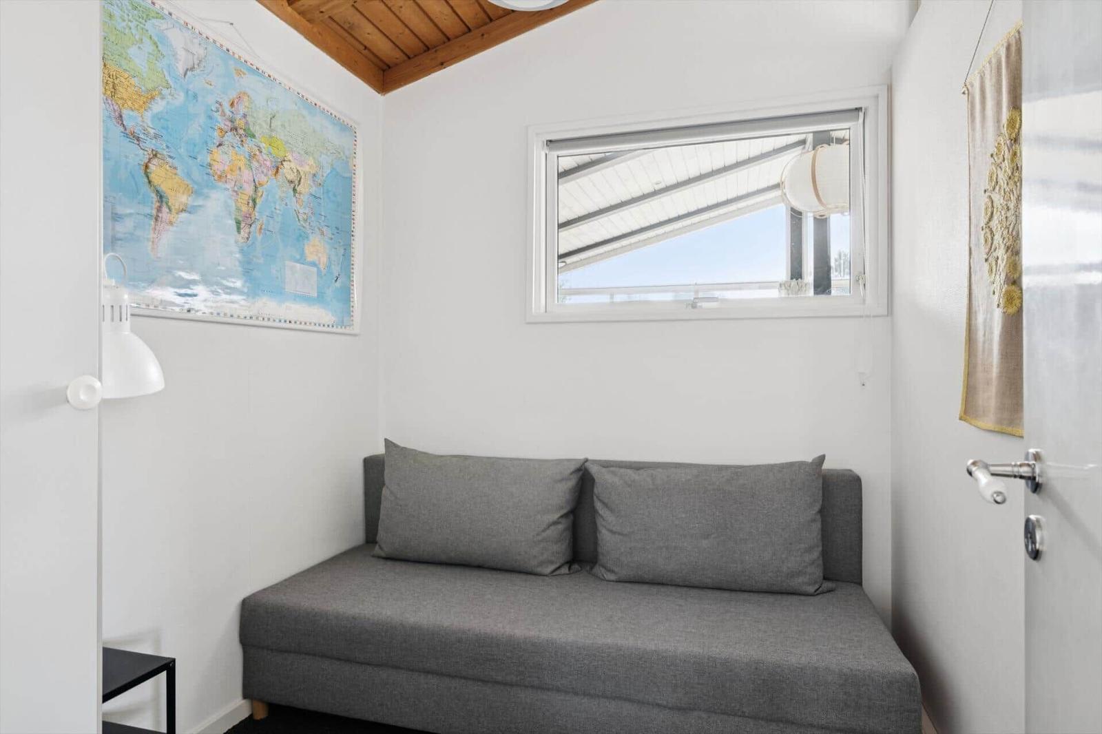 Ein Raum mit grasem Sofa, Weltkarte an der Wand und kleinem Fenster.