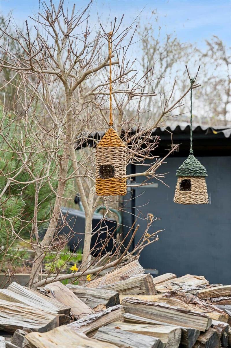 Zwei hängende Vogelhäuser aus geflochtenem Material an einem kahlen Baum im Garten.