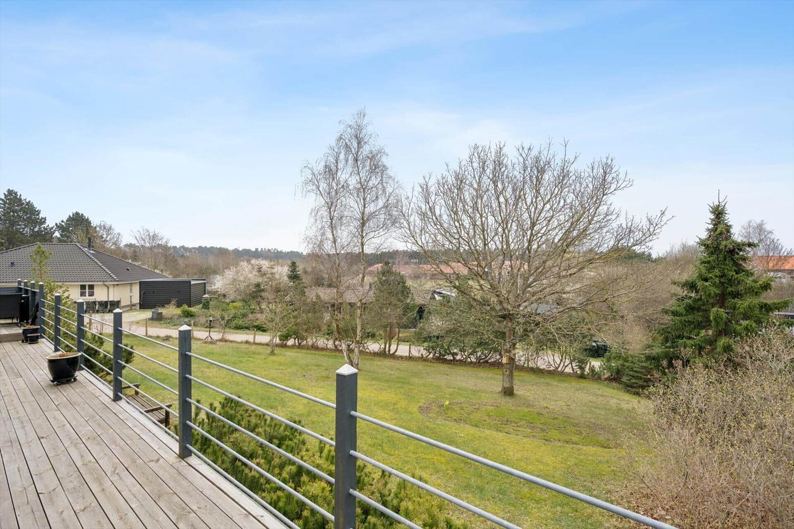 Holzterrasse mit Metallgeländer und Blick auf grünen Garten und Bäume.