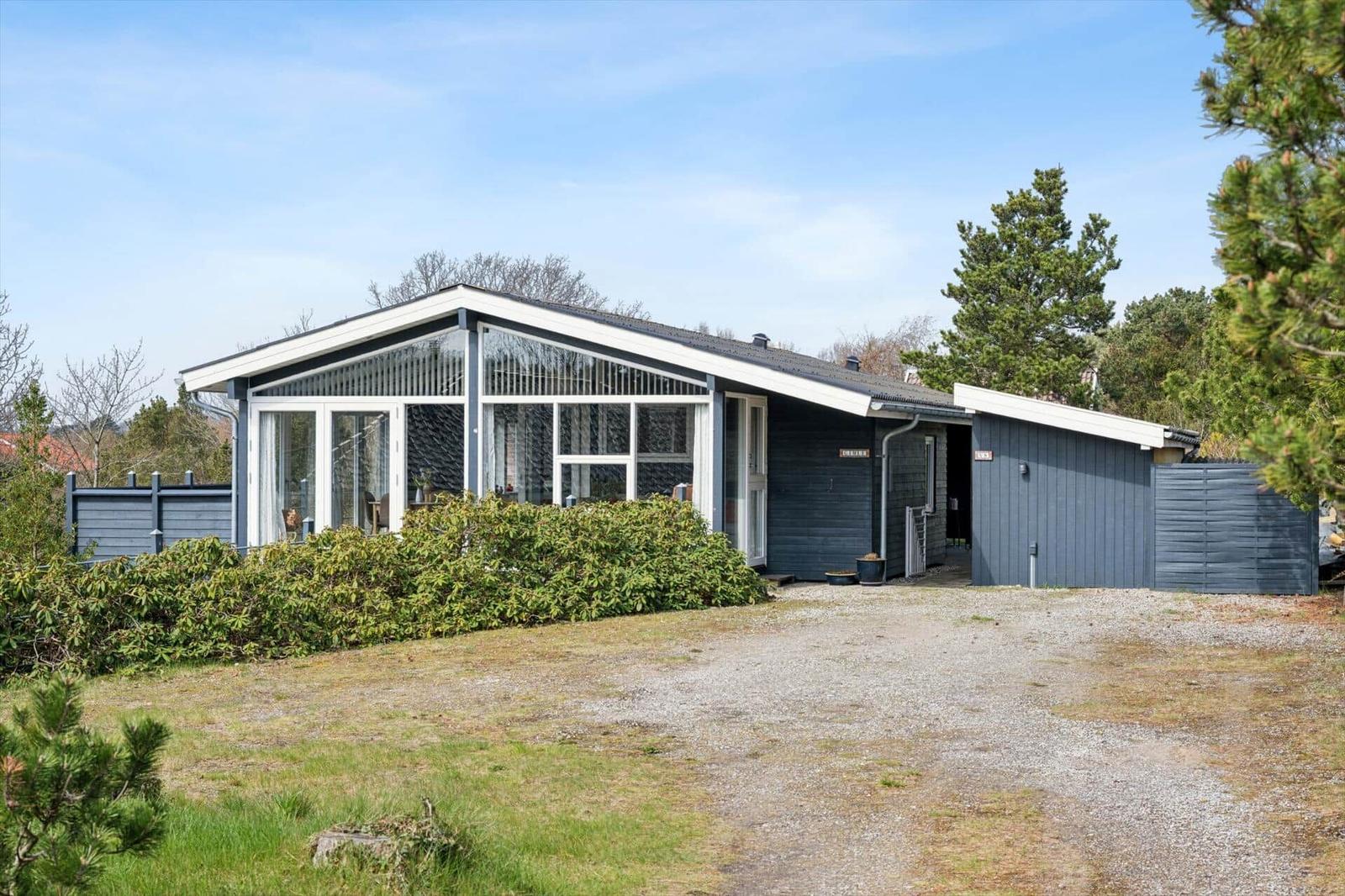 Moderne Villa mit großem Glasbereich und dunkelblauer Fassade. Garten und Parkplatz sichtbar.