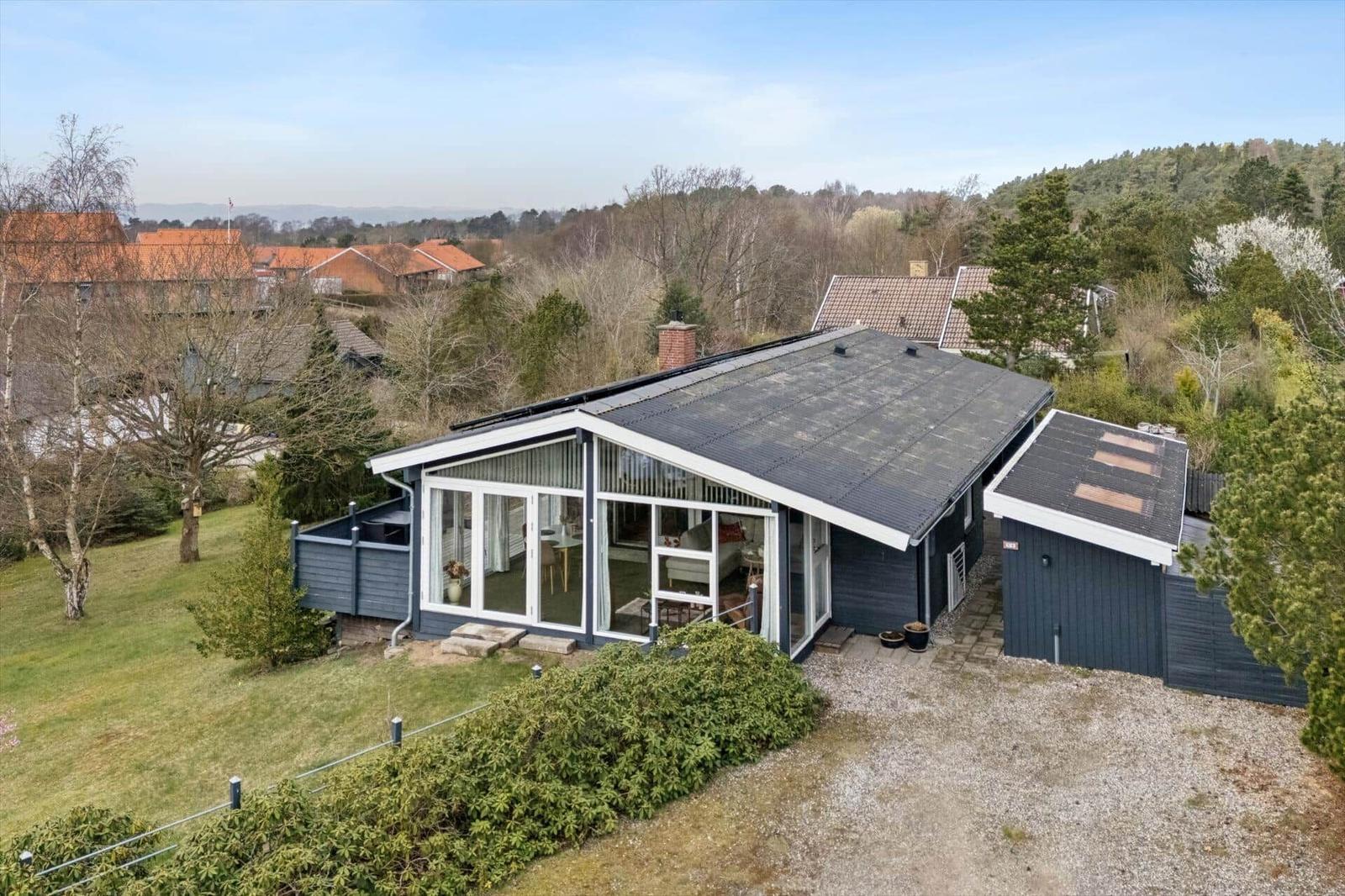 Moderne Villa mit großem Glasbereich und Garten. Blick auf Wald und Nachbarhäuser.